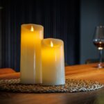 Zestaw 2 ładowalnych świec LED z wosku DORSETTO na plecionej podkładce, z kieliszkiem czerwonego wina i butelką w tle – przytulna, elegancka atmosfera